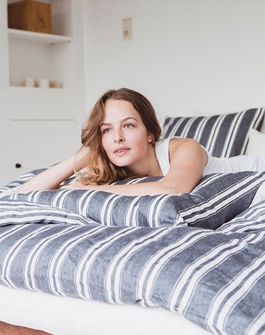 Woman laying on a bed with gray and white striped blankets and pillows