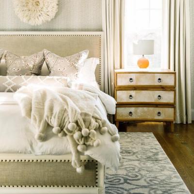 Bedroom showing a bed with white sheets, throw pillows and headboard with an end table and rug